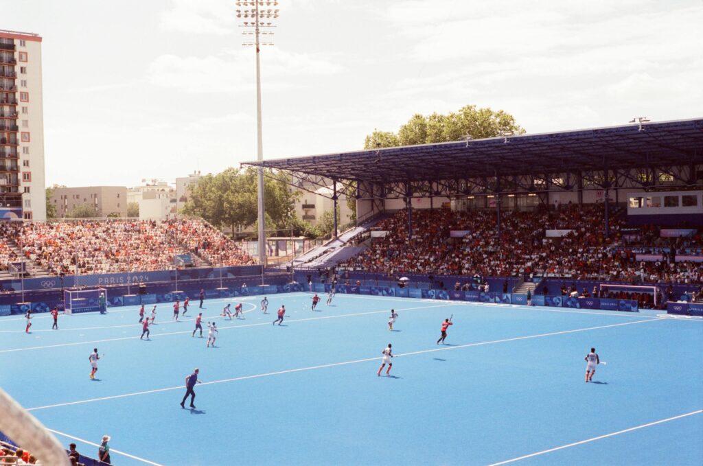 Field hockey match in a vibrant stadium during Paris 2024 event, showcasing athlete action and large crowd.