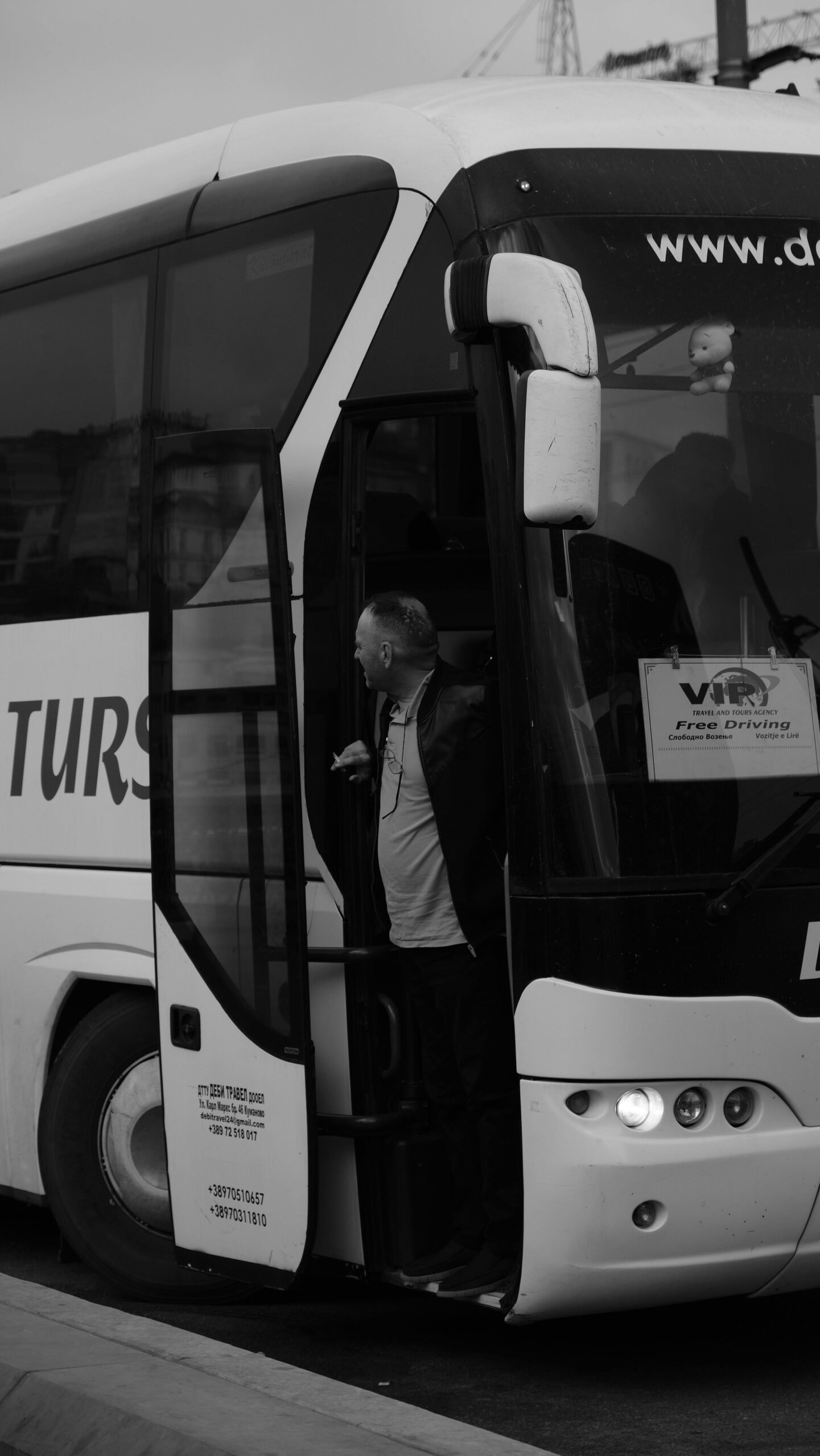 Monochrome photo of a man exiting a tour bus on a city street.