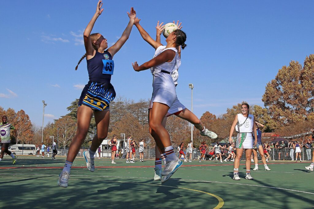Dynamic capture of a netball match on a sunny day, featuring female athletes in action.